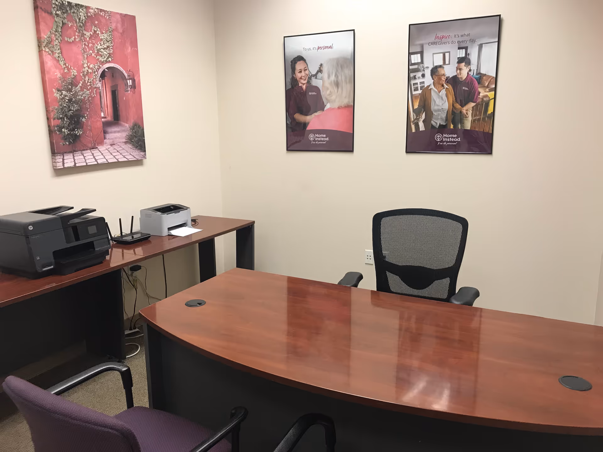 A polished curved wooden reception desk in a small office with printer and framed posters.