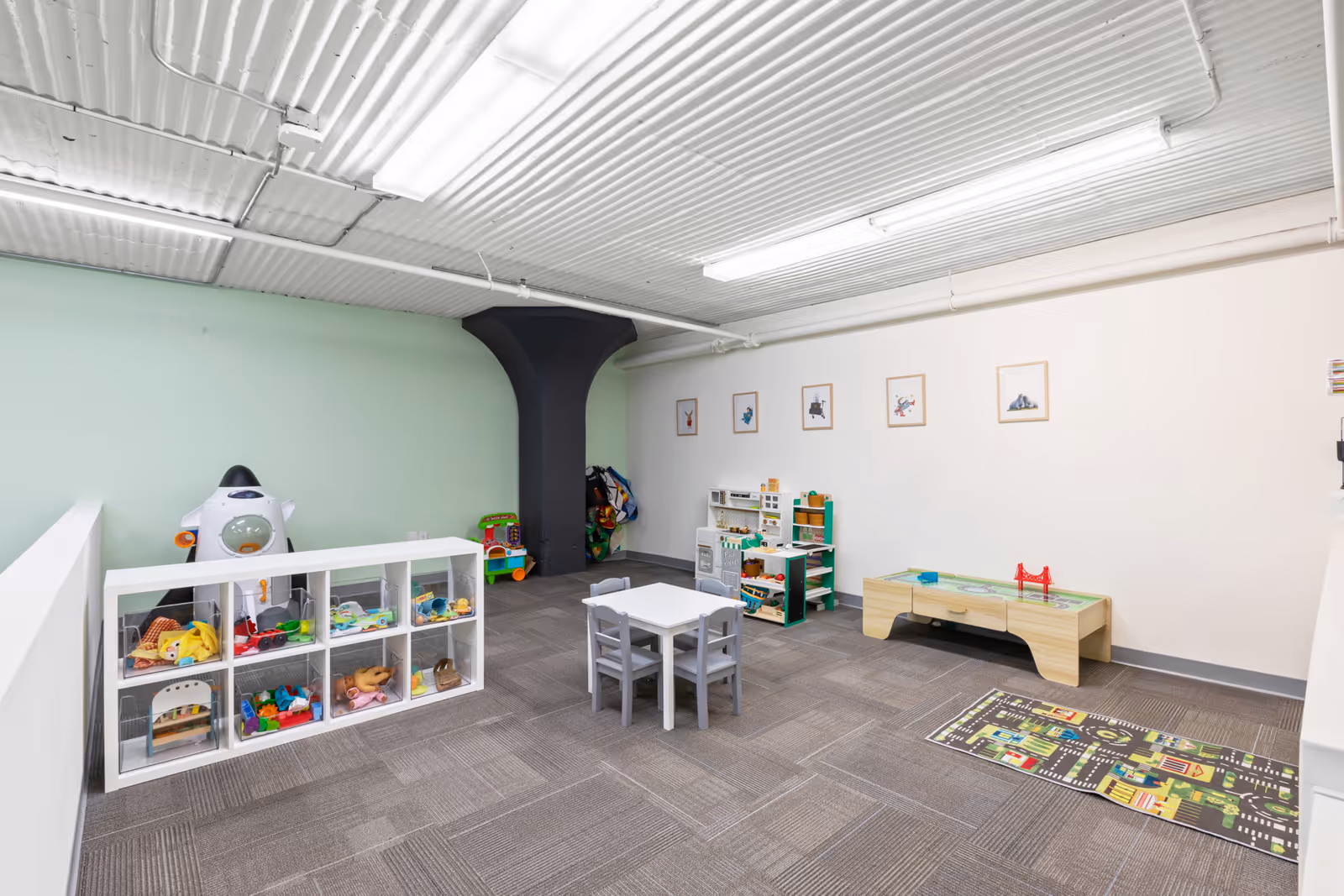 Indoor playroom with toy shelves, small table and chairs, and activity mats.