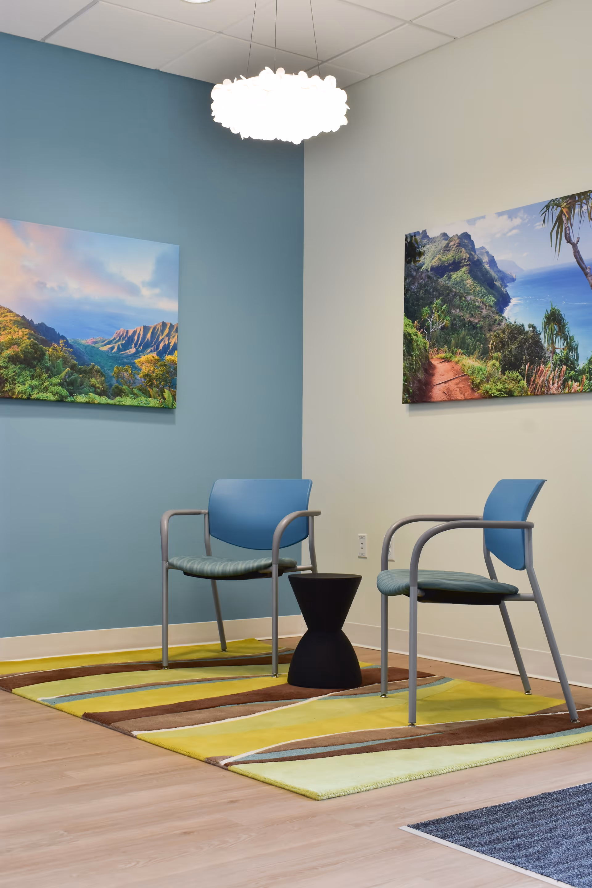 Two blue chairs with a small black side table in a bright waiting area.