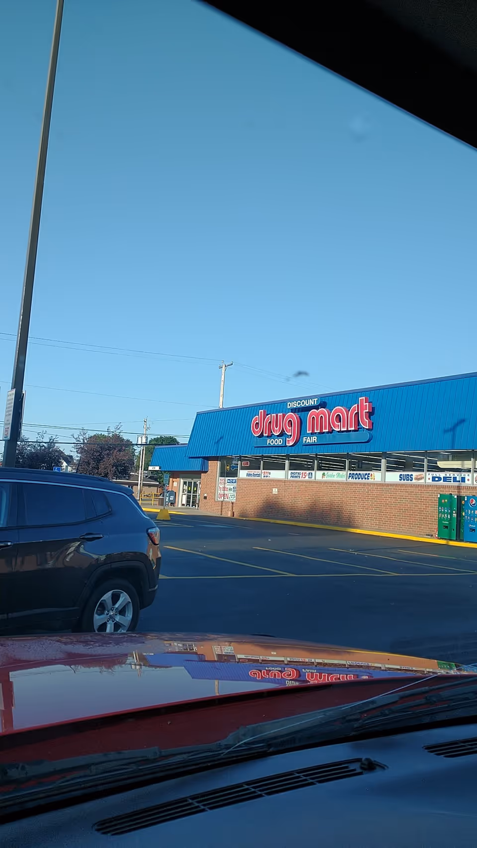 Blue Discount Drug Mart storefront with parking lot and vehicles in foreground.