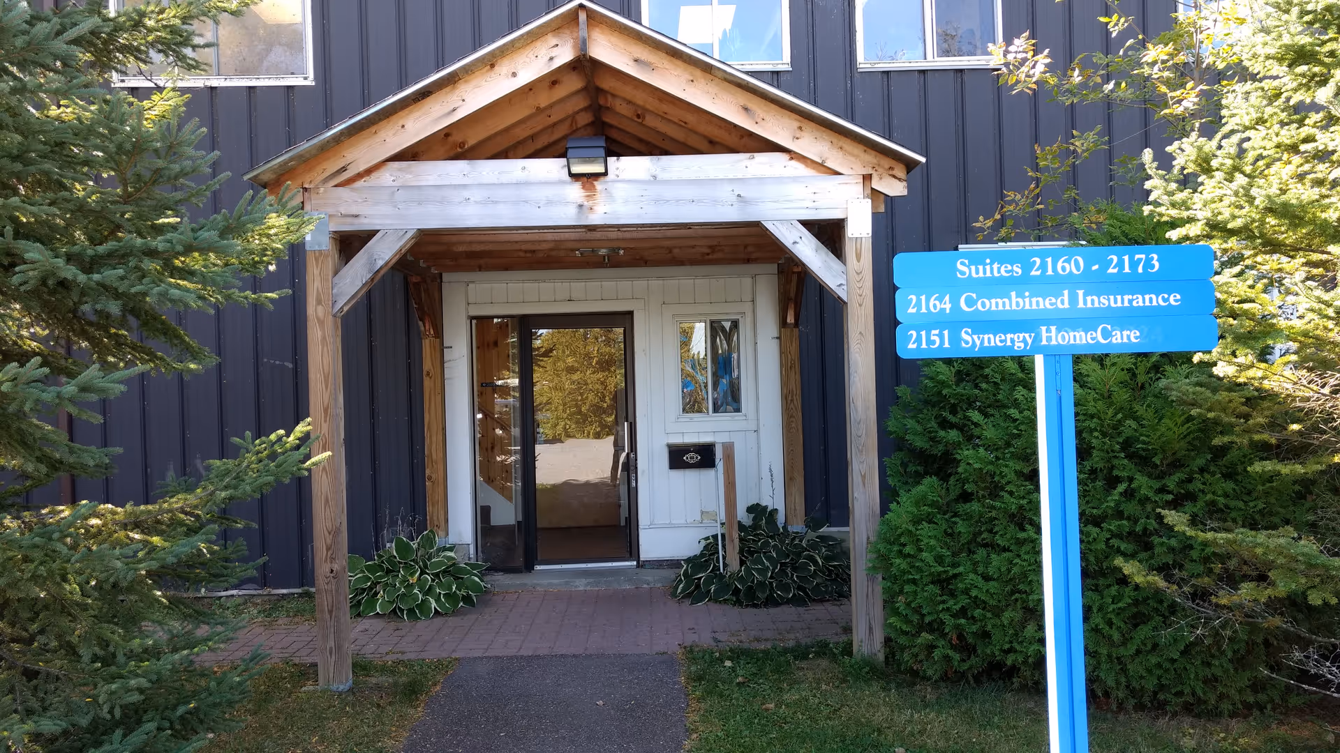 Exterior entrance of a Synergy HomeCare facility with a wooden porch and blue sign.