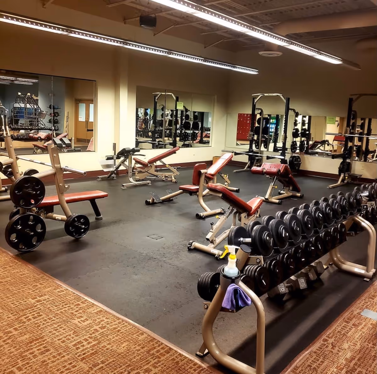 Indoor senior living gym with weight benches, dumbbells, and mirrors.