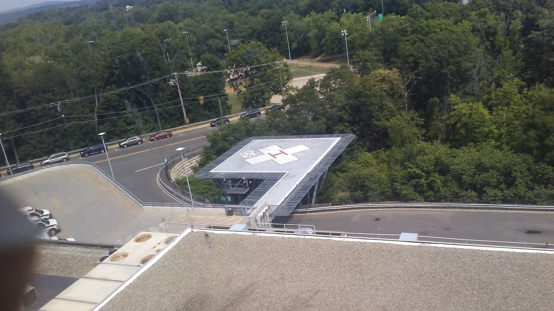 Aerial view of Middlesex Hospital rooftop with a helipad, road, and surrounding trees.