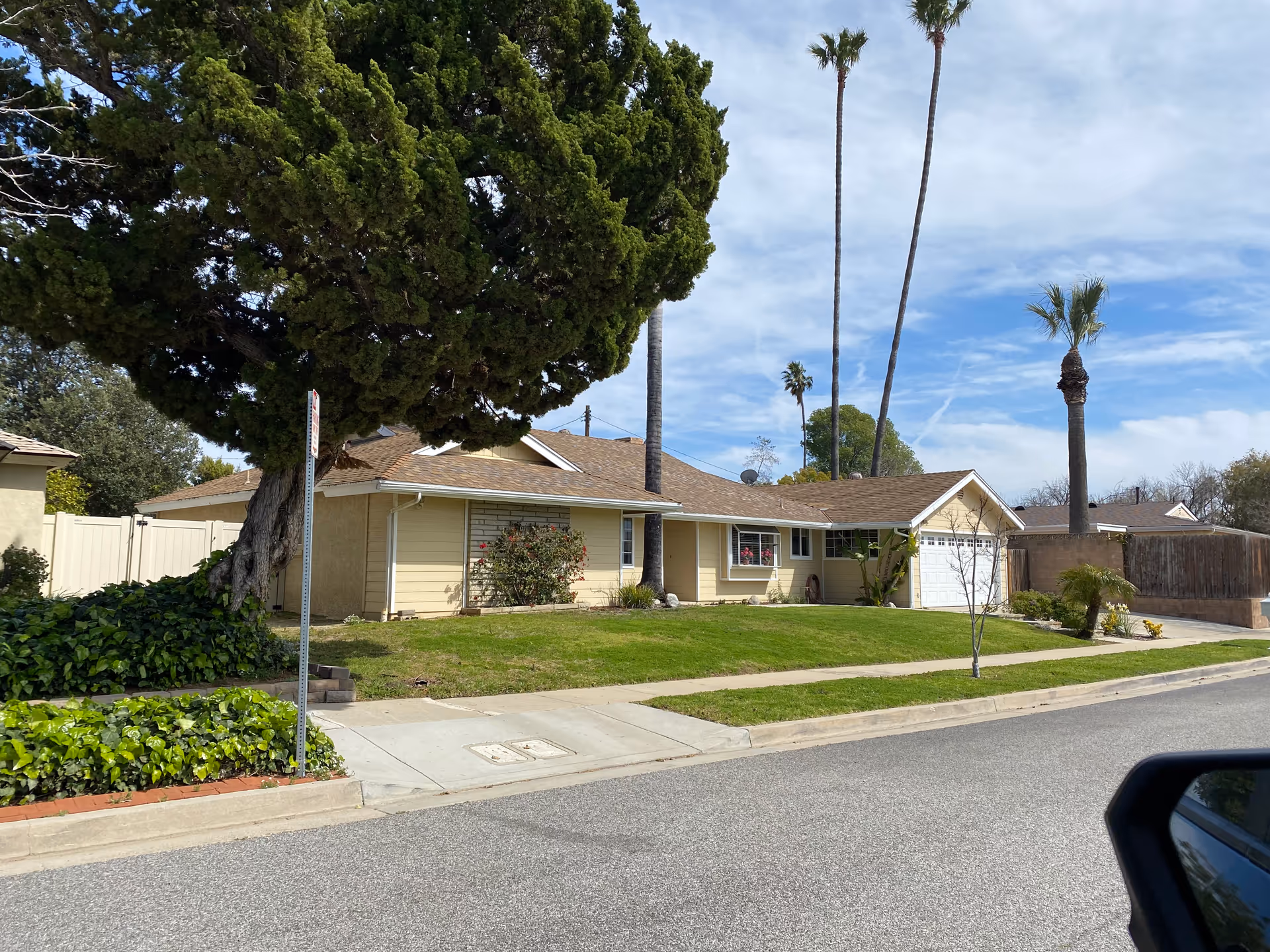Front view of a single-story beige house with a manicured lawn and palm trees.
