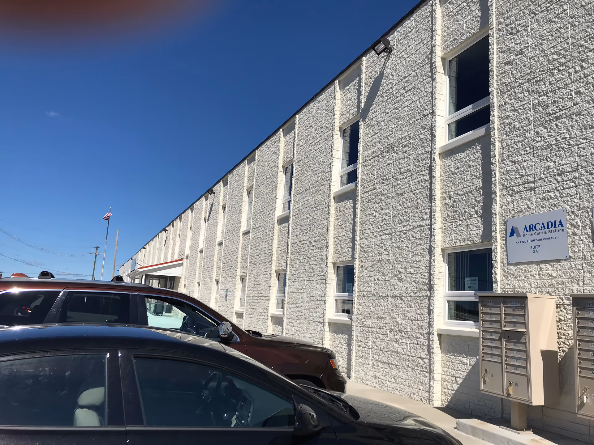 White brick building exterior with parked cars and Arcadia Home Care & Staffing sign.