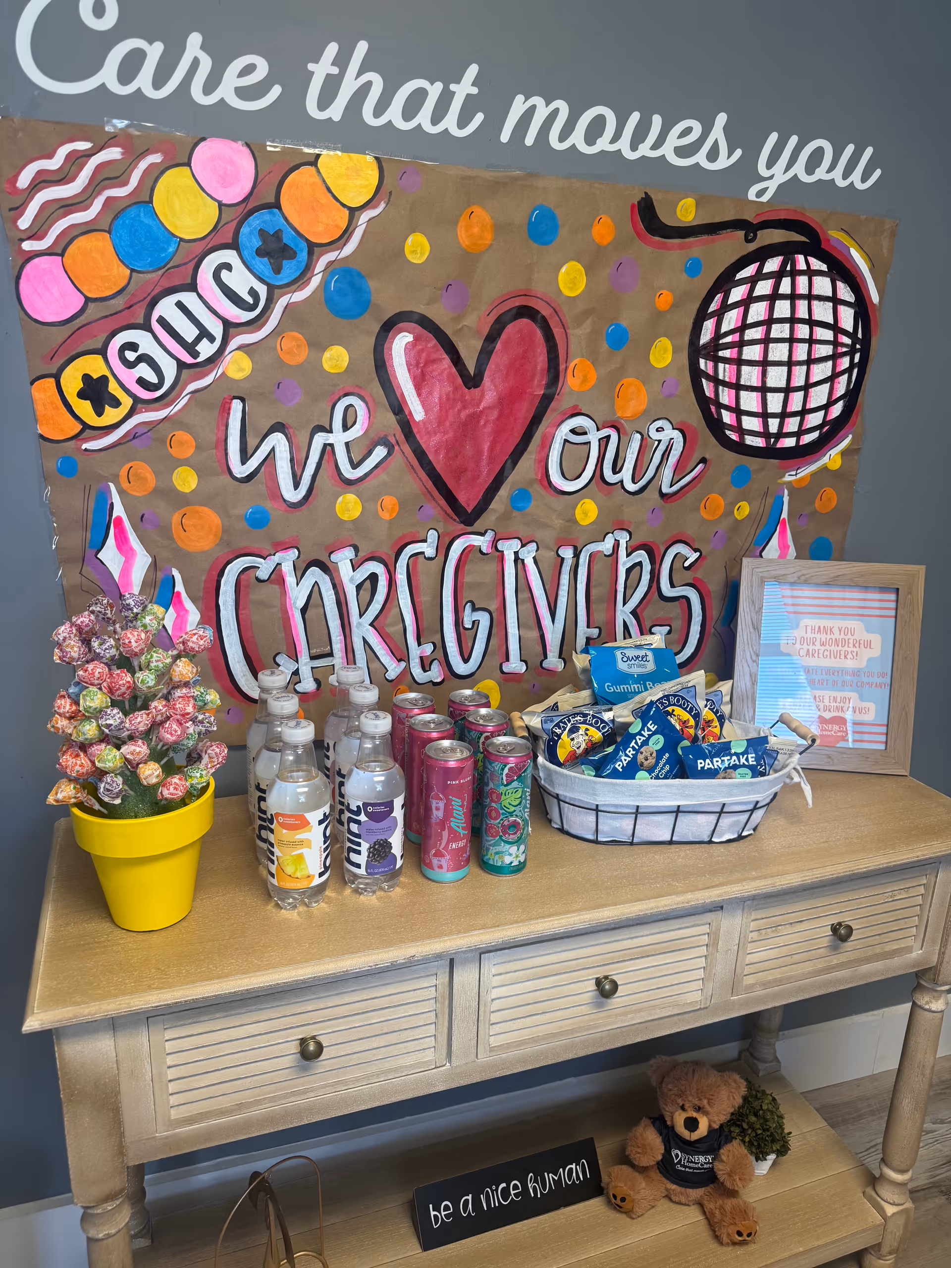 Decorative sideboard display in a senior care setting with beverages, snacks, and a caregiver appreciation banner.