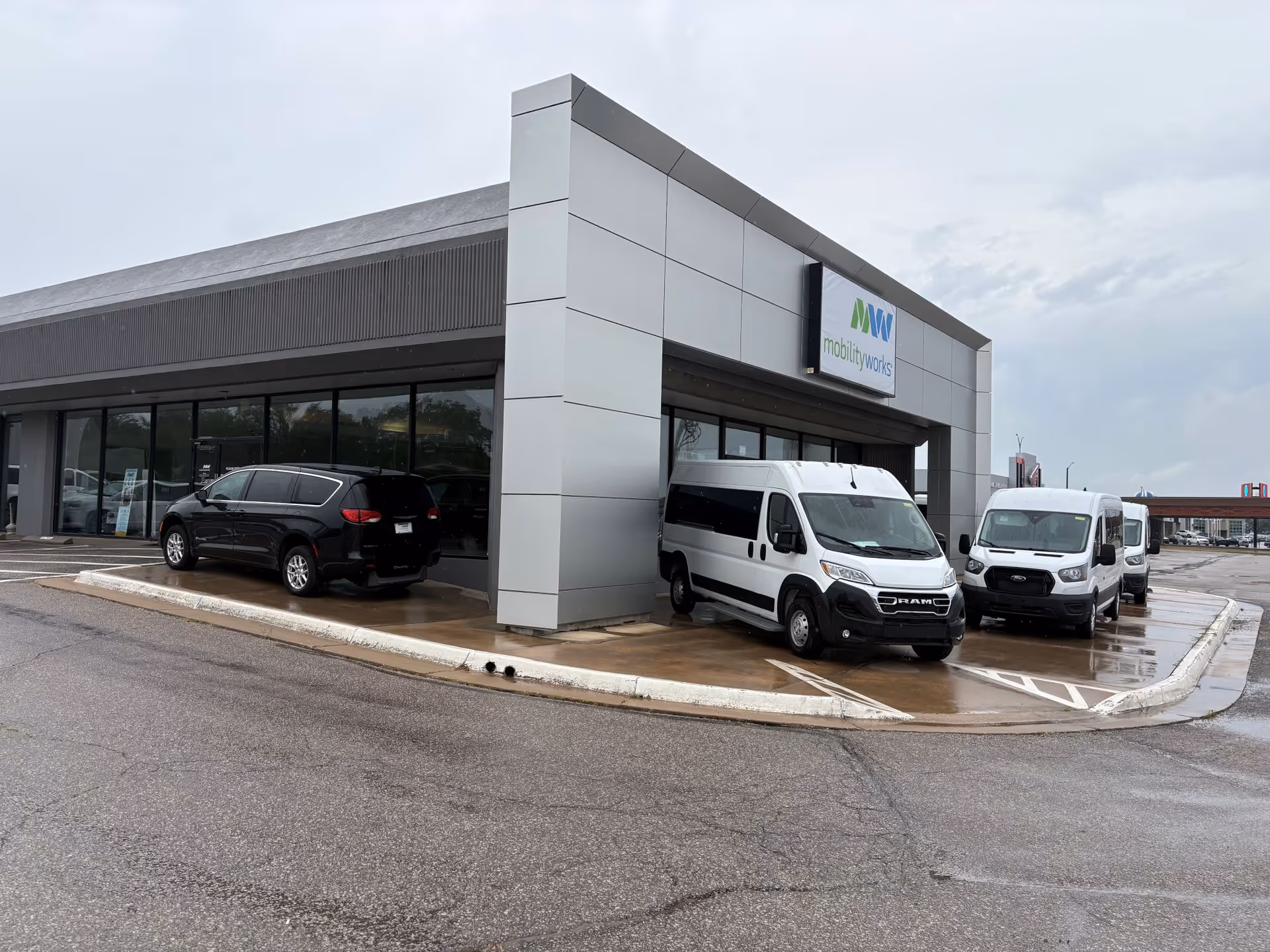 Modern MobilityWorks building with white vans parked along the wet pavement.