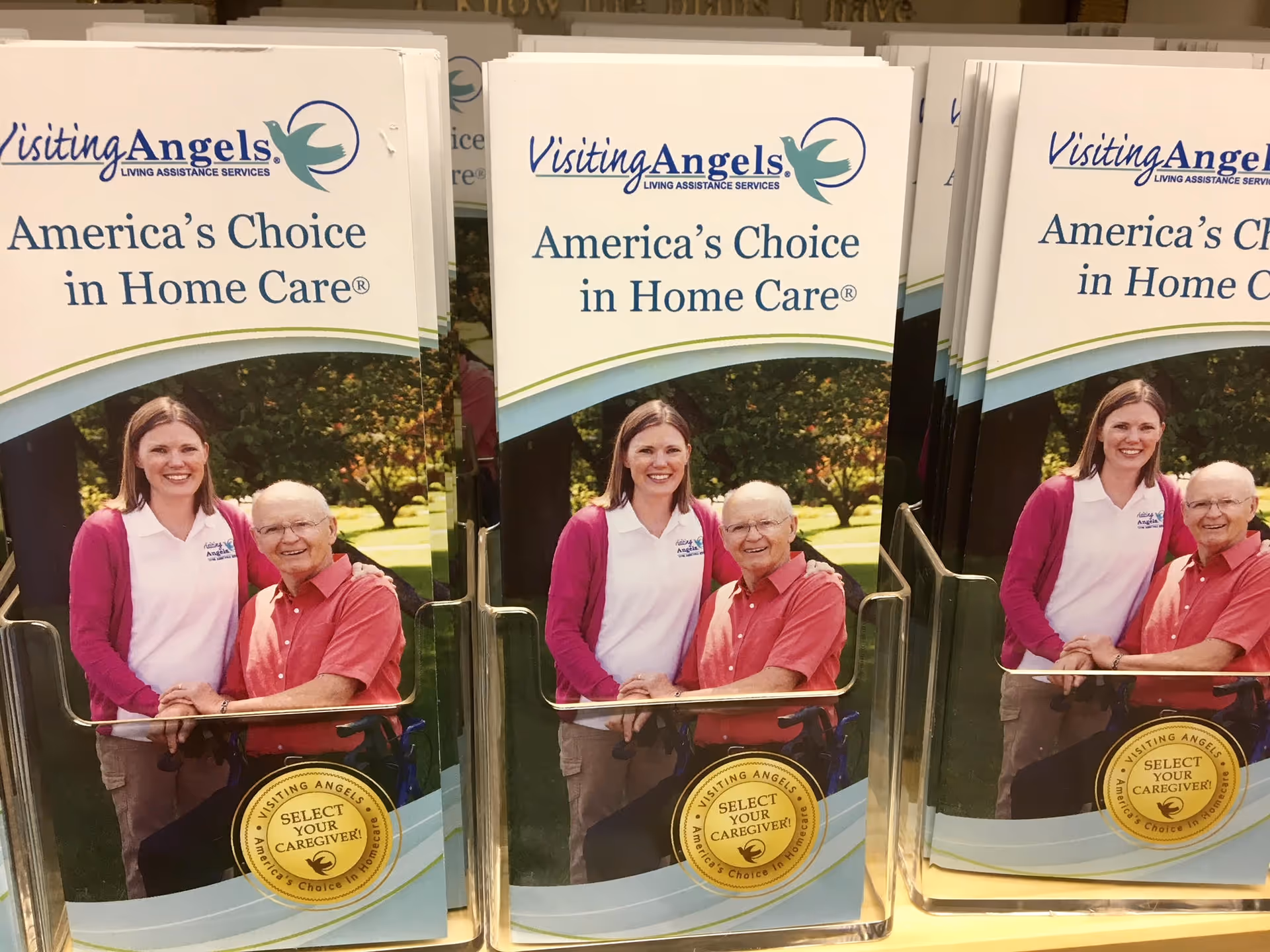 Three Visiting Angels brochures on a rack featuring a caregiver and senior on the cover.