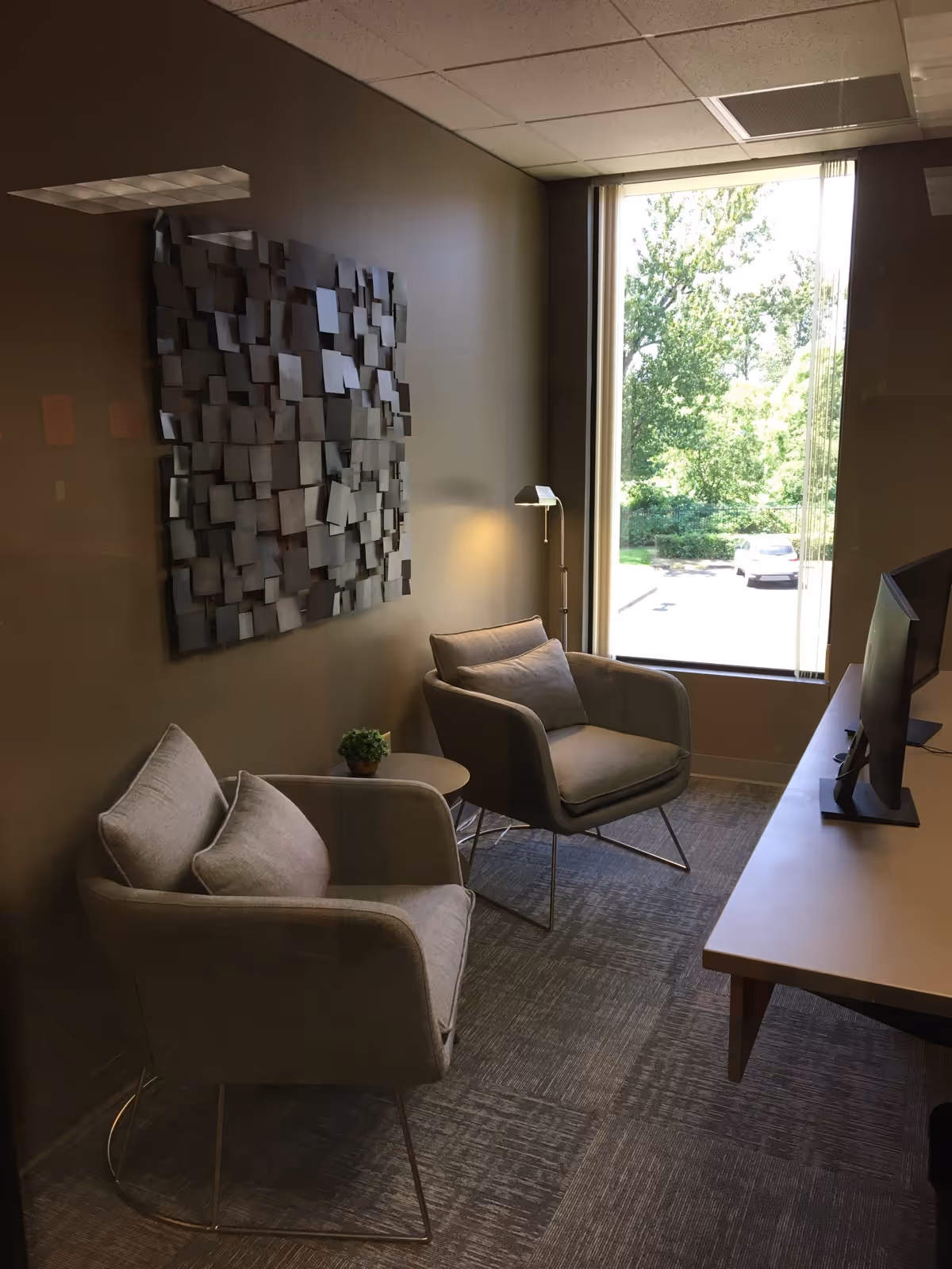 A small modern waiting area with two gray chairs, wall art, and a desk.