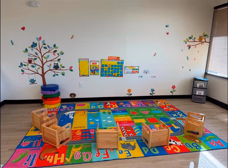 Colorful children's therapy room with wall mural, alphabet rug, and small wooden chairs.