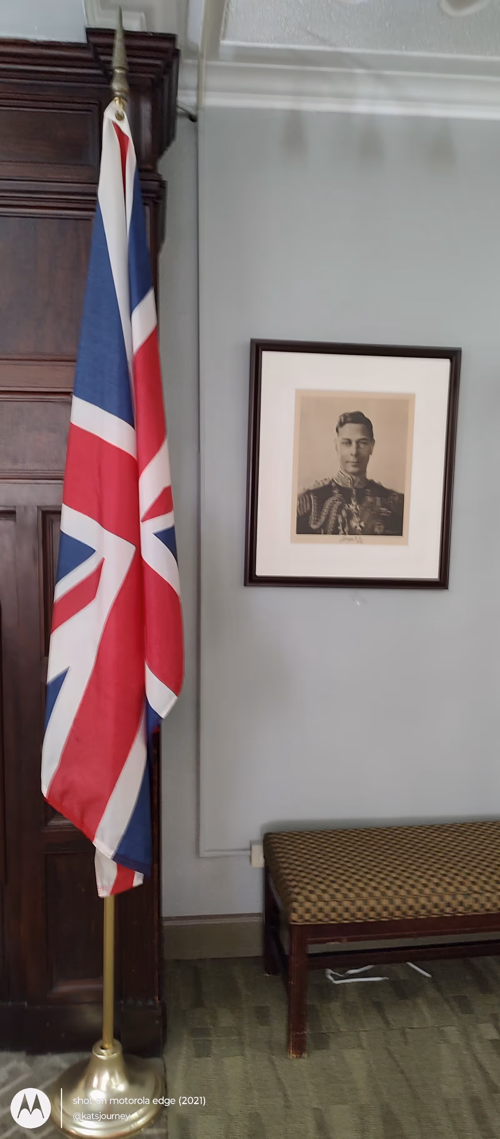 Union Jack flag beside a framed portrait in a neutral interior room.