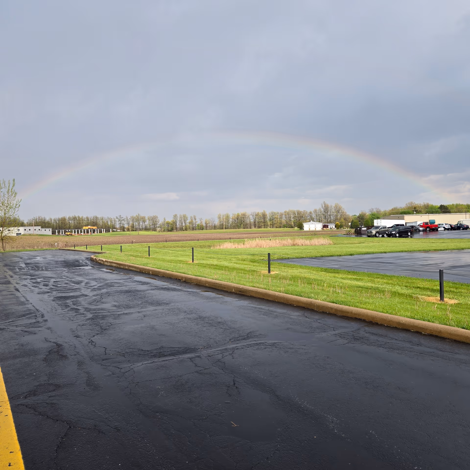 Exterior view of a parking lot and grassy fields with a distant rainbow overhead.