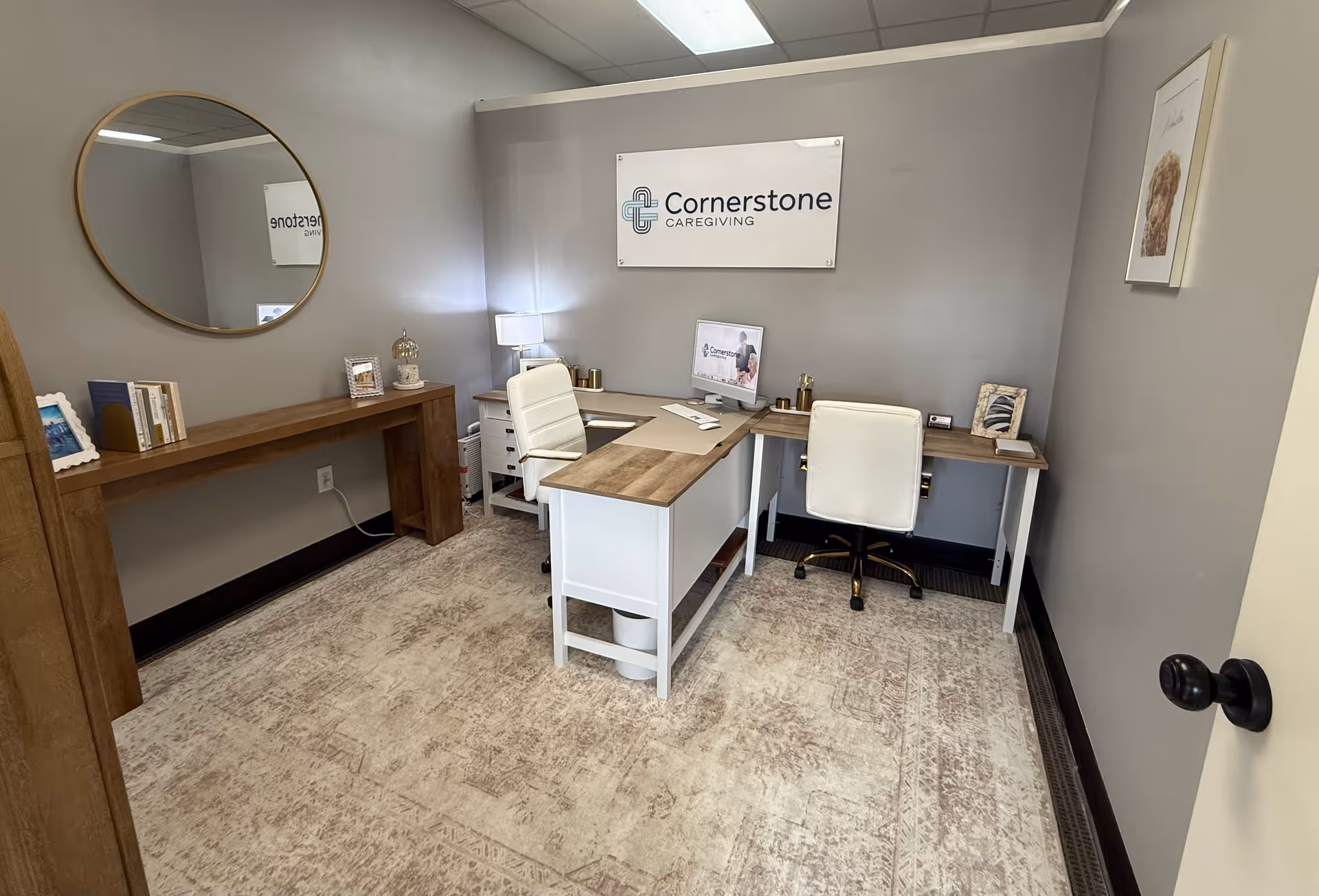 Office reception area with a desk, chairs, and a Cornerstone Caregiving banner on gray walls.
