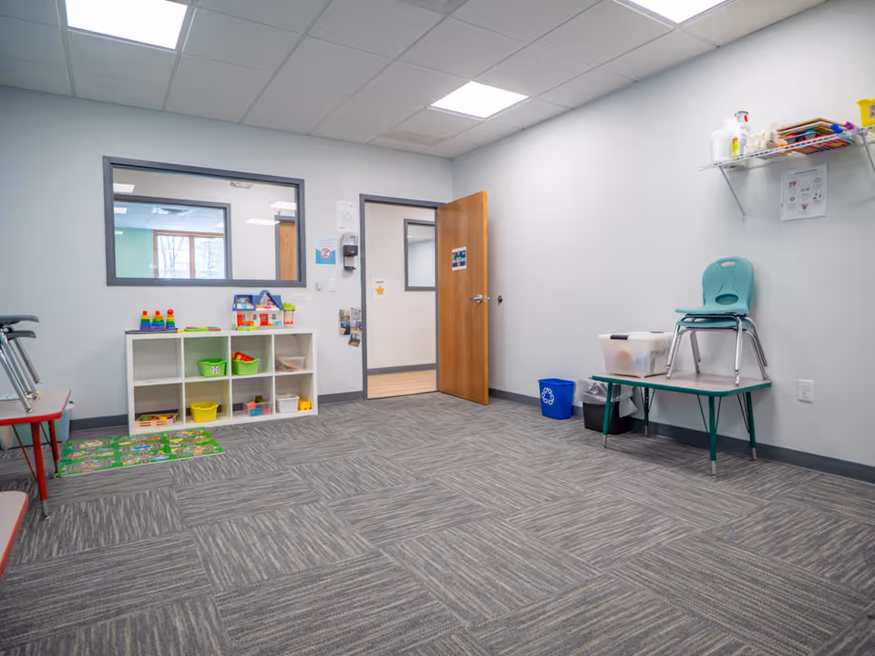 Bright therapy playroom with toy shelves, mats, and a doorway.