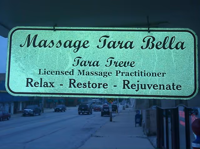 Green signage reading Massage Tara Bella hangs over a street storefront.