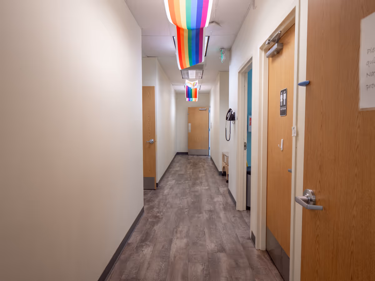 Interior hallway in a senior living facility with doors and rainbow ceiling banners.