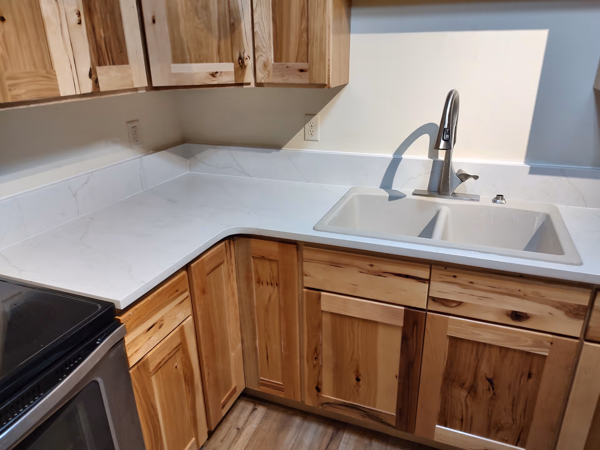 Wooden kitchen with light countertops, upper cabinets, and a double sink.