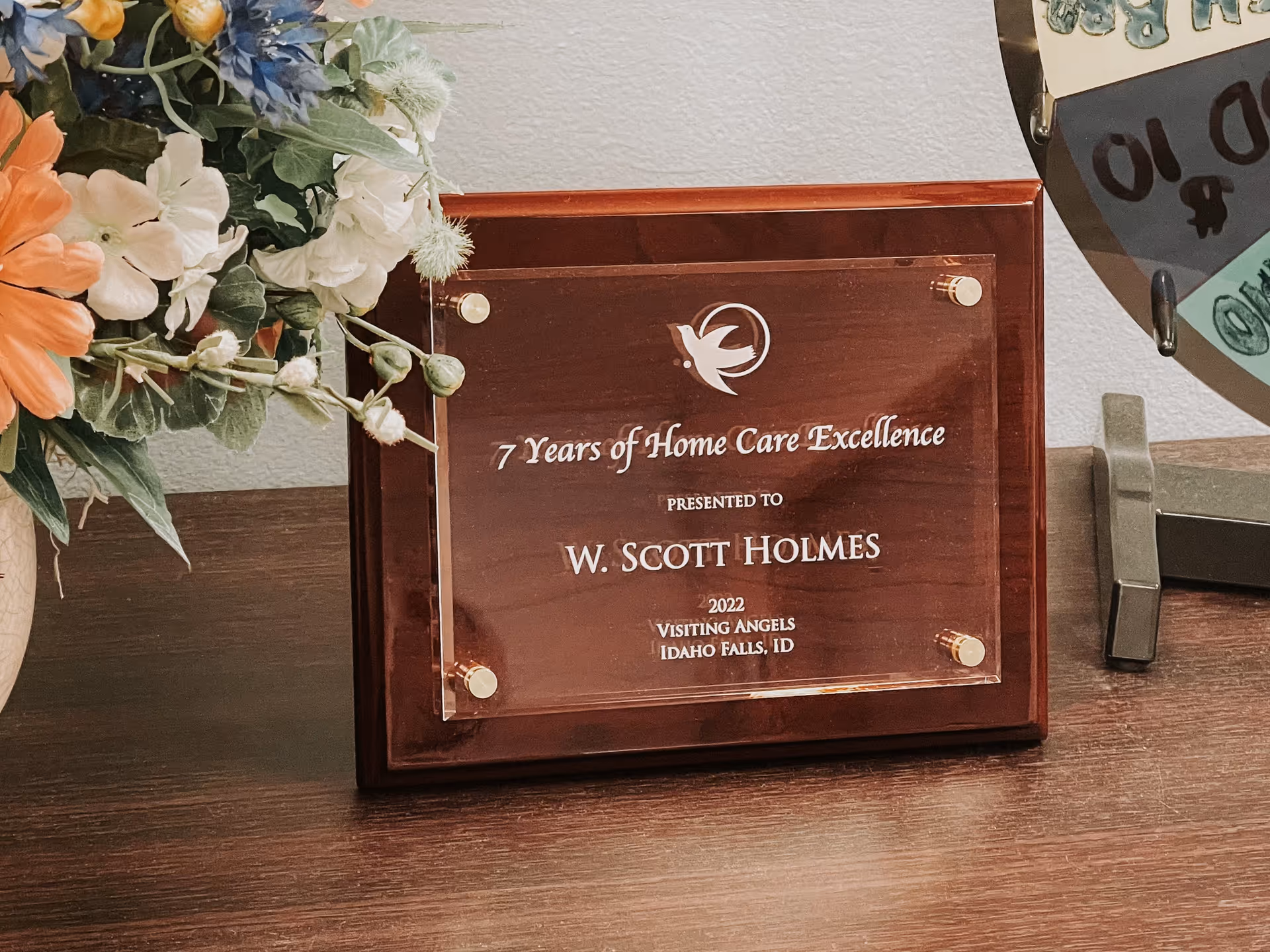 Wooden award plaque on a desk with flowers, inscribed 7 Years of Home Care Excellence.