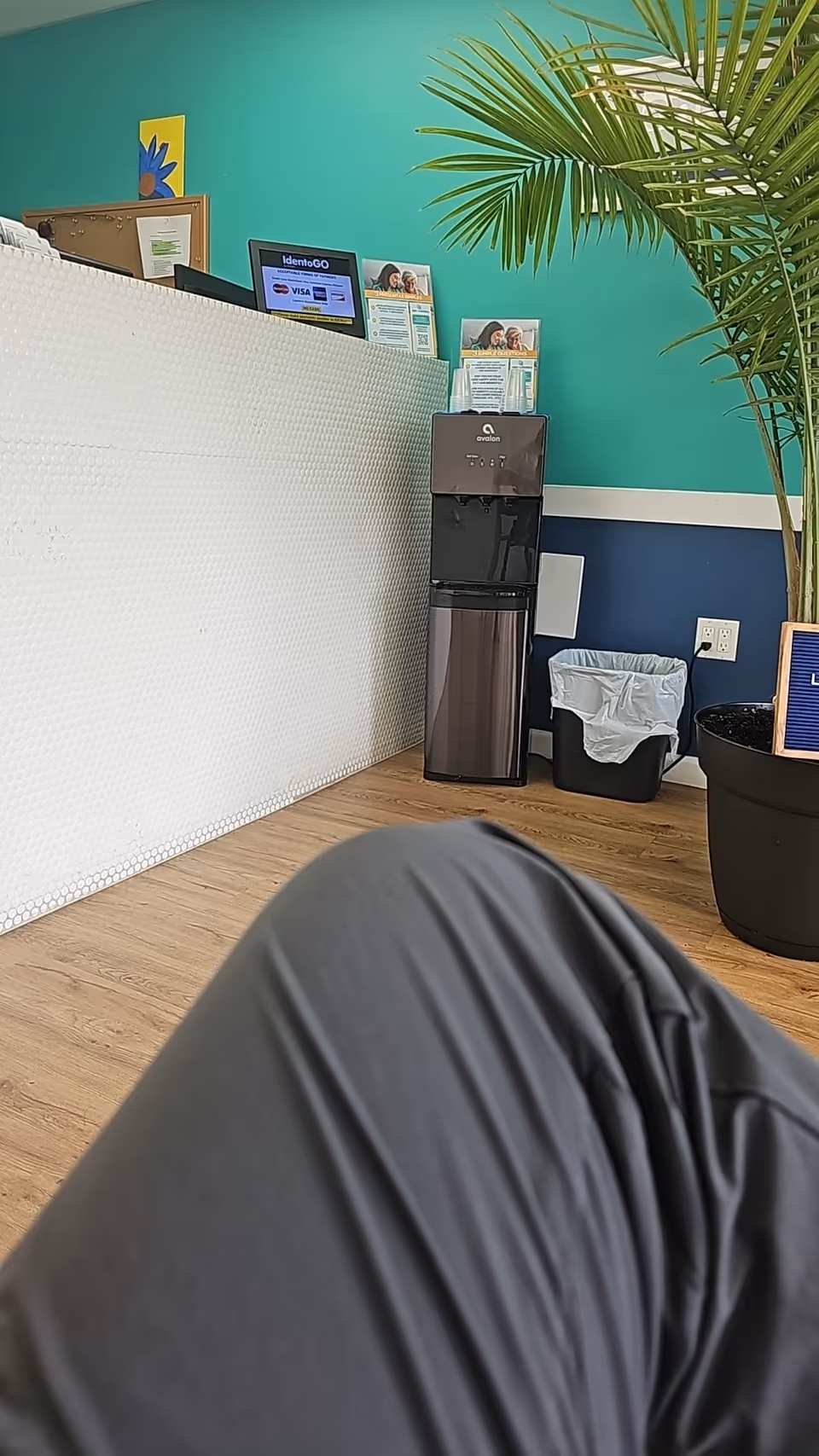 Reception desk in a bright teal lobby with a water cooler and plants.