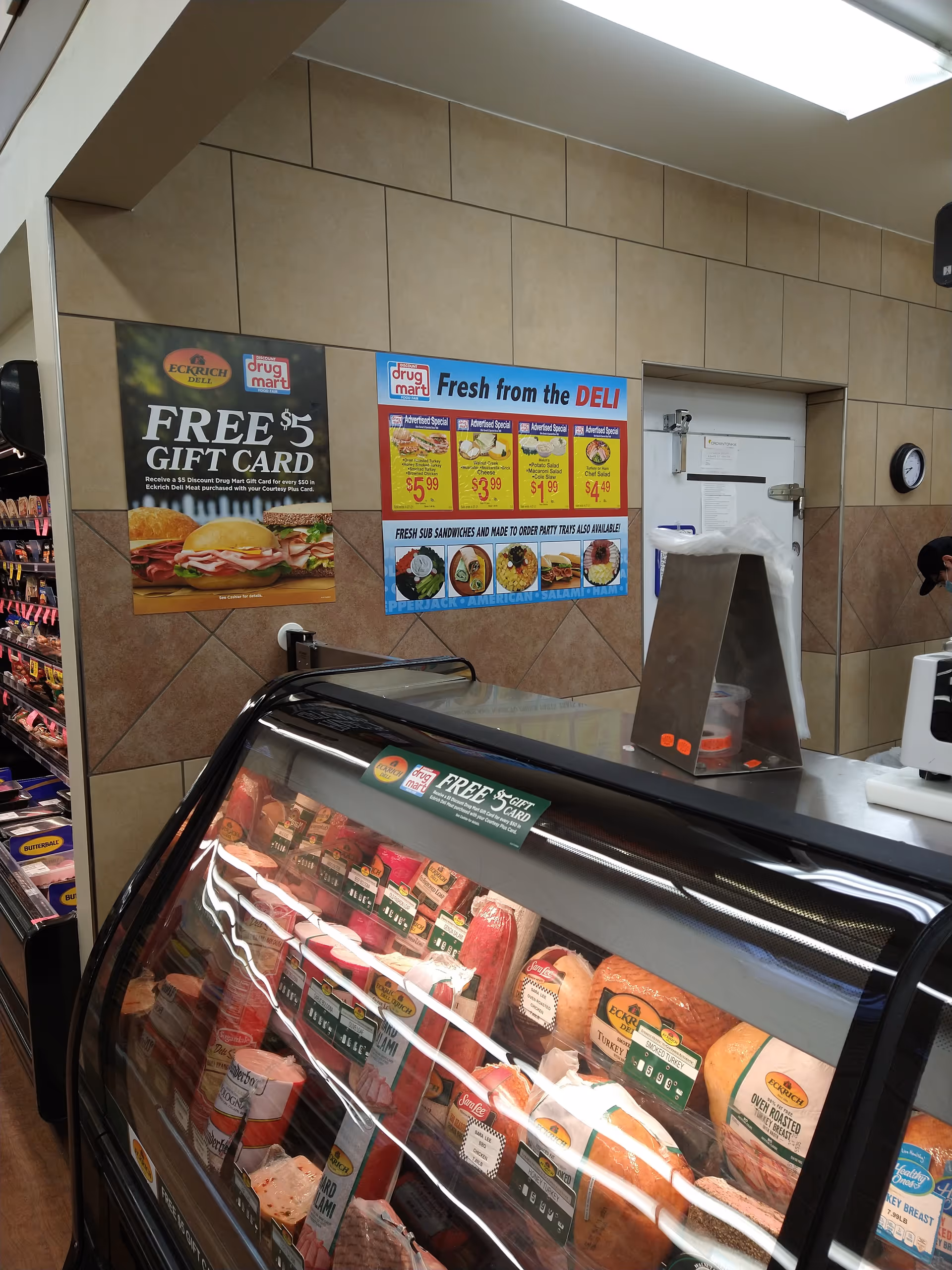 Deli counter inside Discount Drug Mart with meat display and posters.