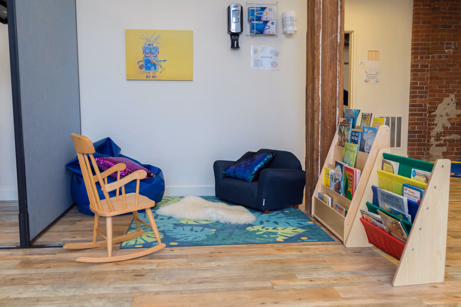 Cozy indoor seating area with wooden rocking chair, blue sofa, rug, and brochure rack.