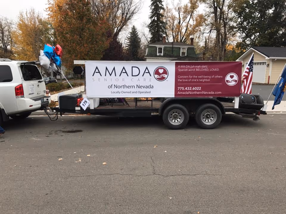 A trailer displays Amada Senior Care banner and balloons parked on a suburban street.
