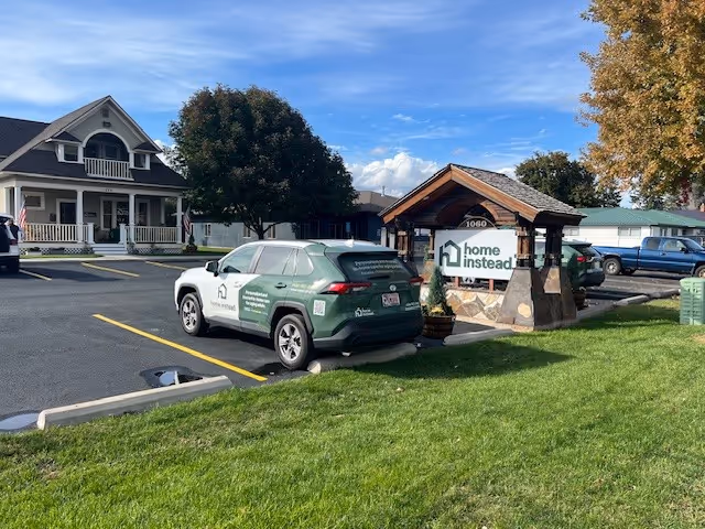 Exterior view of a Home Instead facility with a green service vehicle and entrance sign.