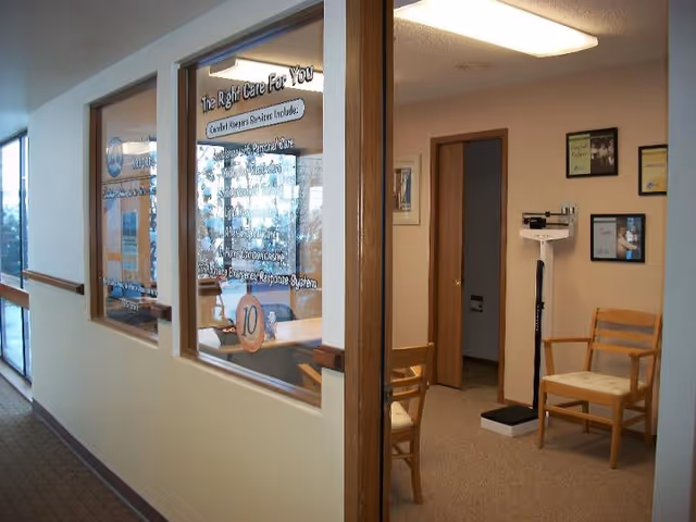 Interior hallway of Comfort Keepers Home Care with glass-walled rooms and wooden chairs.