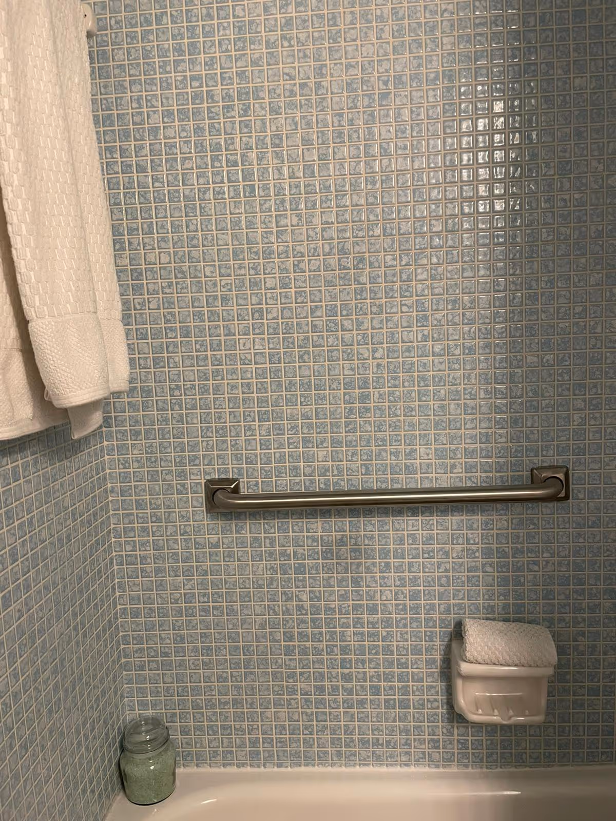 Blue mosaic-tiled bathroom with towel, grab bar, and soap holder by tub.