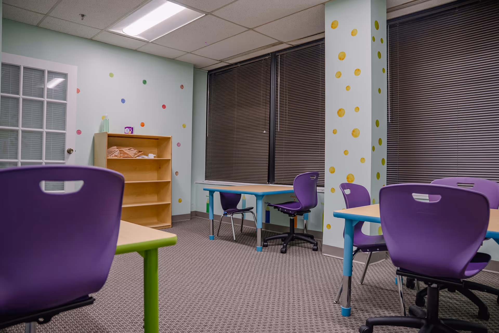 Interior view of a colorful activity room with purple chairs, tables, and polka-dotted walls.