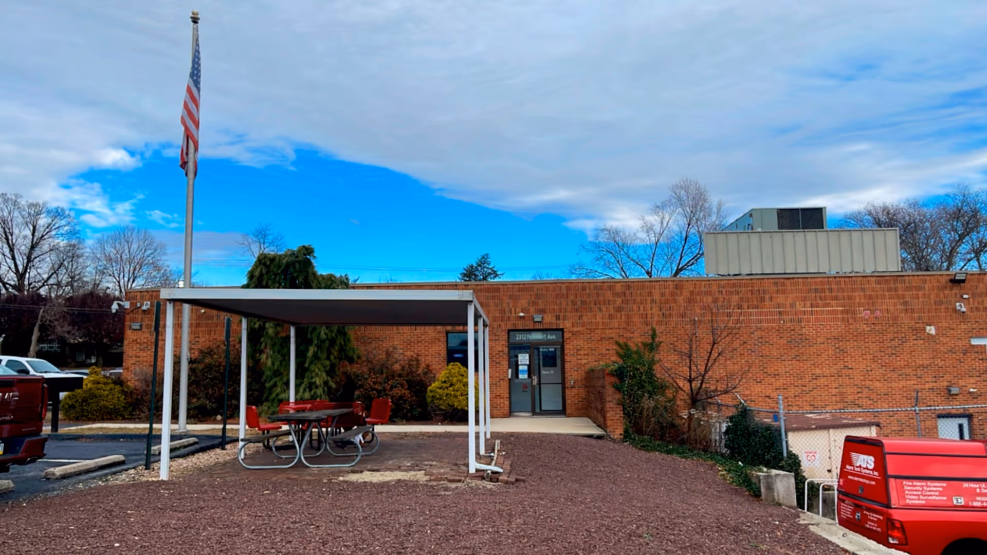 Brick facility exterior with a covered outdoor seating area and American flag.