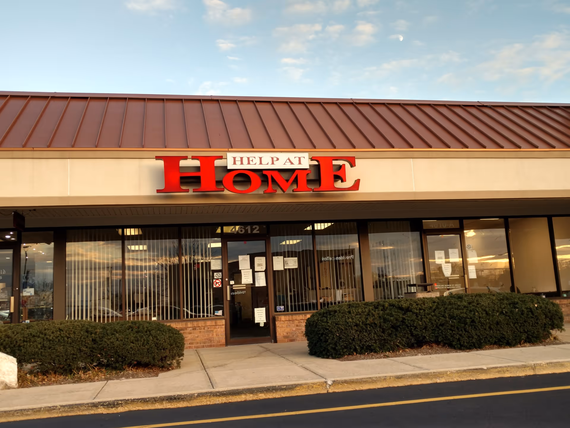 Front view of a Help at Home facility with large red sign and glass storefront.