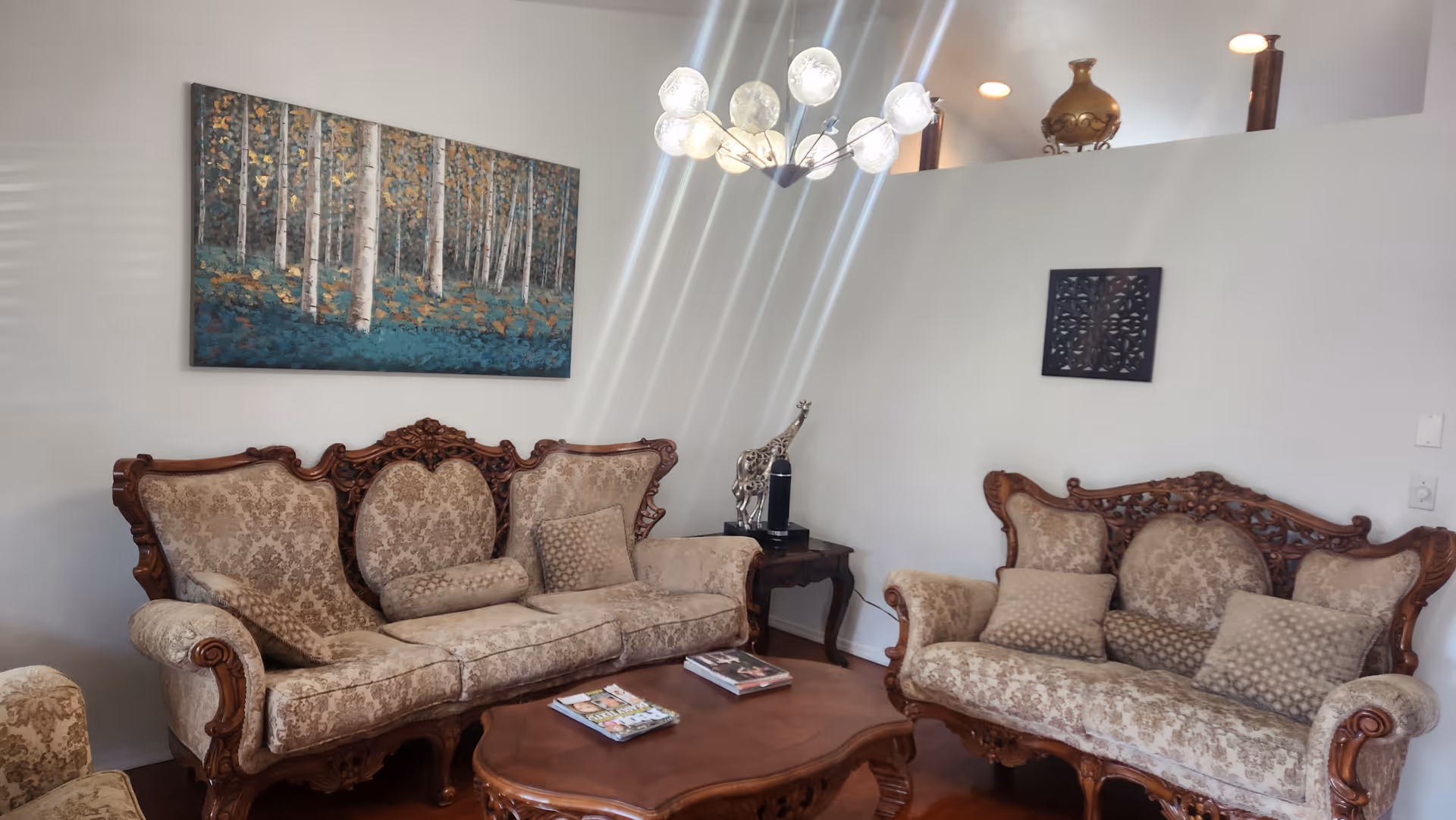 Elegant living room with ornate wooden furniture, a coffee table, chandelier, and wall art.
