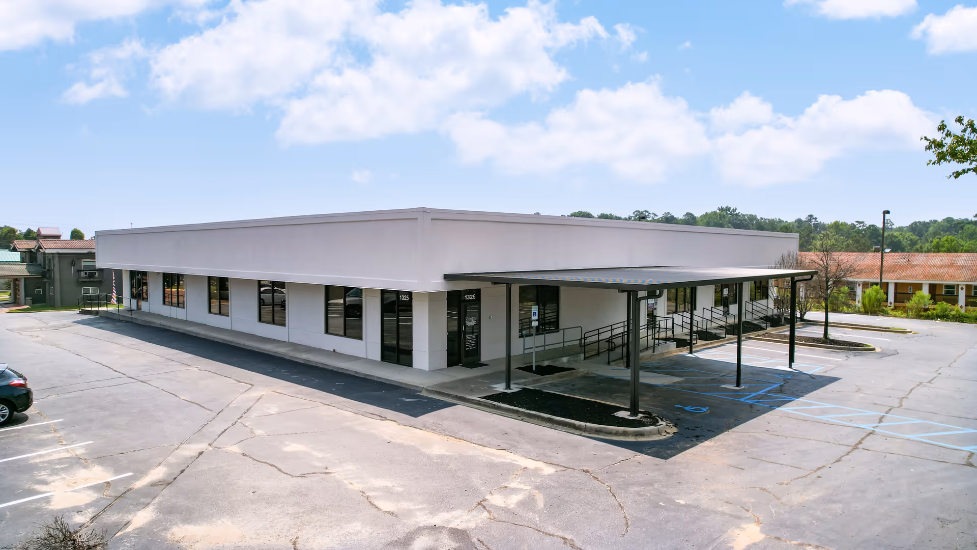 Wide exterior view of a single-story white facility with a covered entrance and parking.