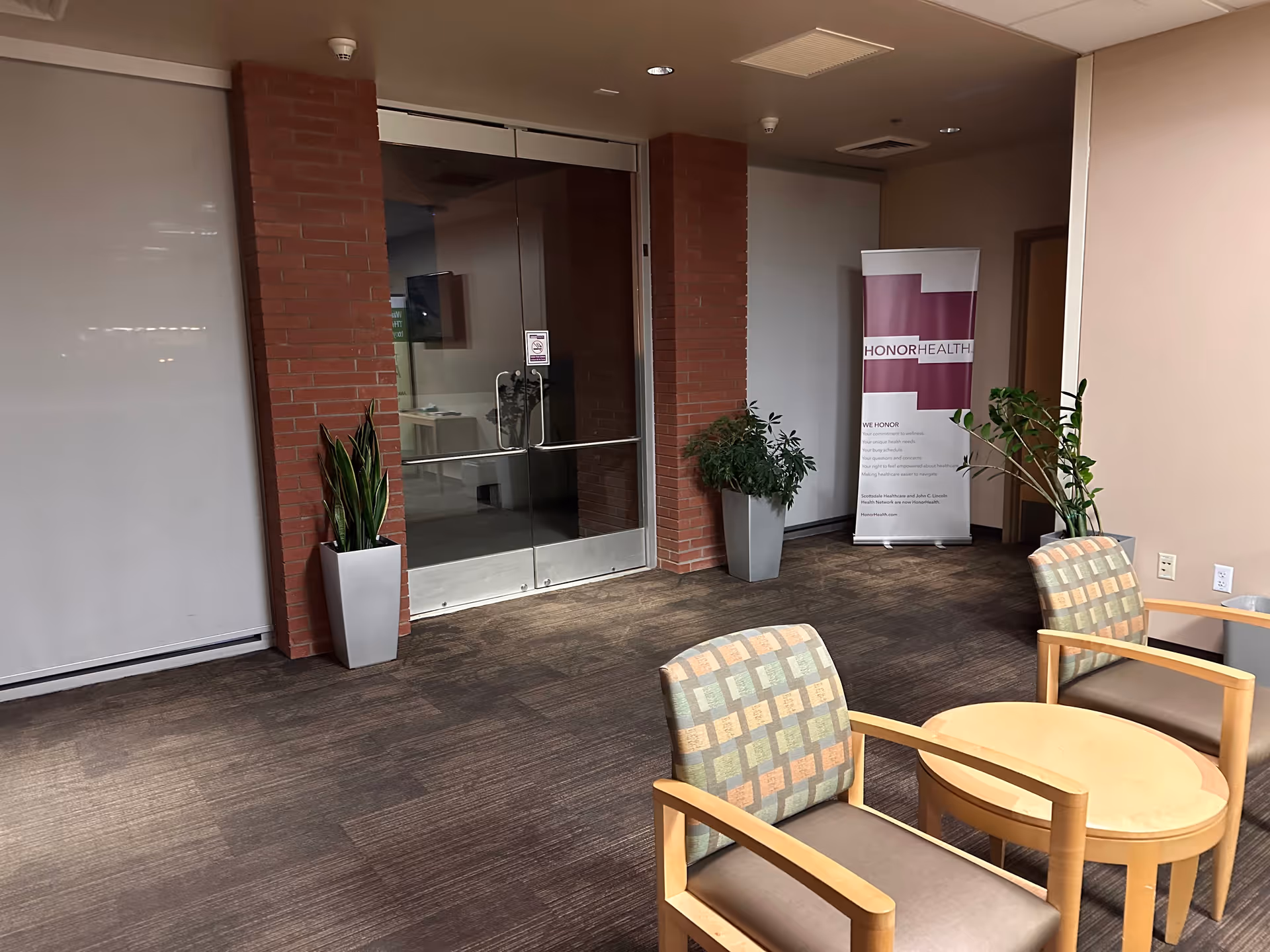 Interior lobby with glass doors, brick columns, and potted plants surrounding seating.