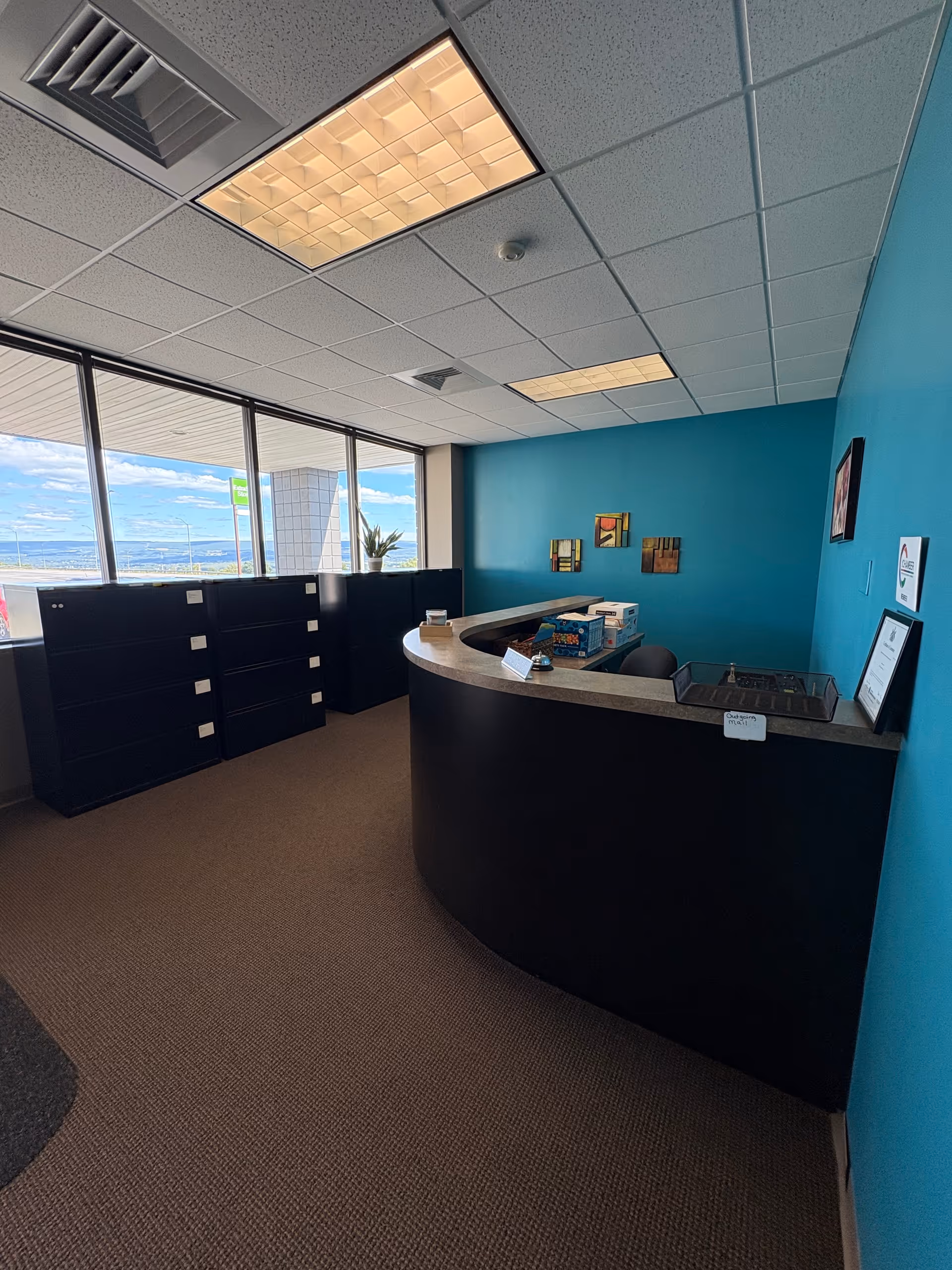 Curved front desk in teal-walled reception area with filing cabinets and large windows.