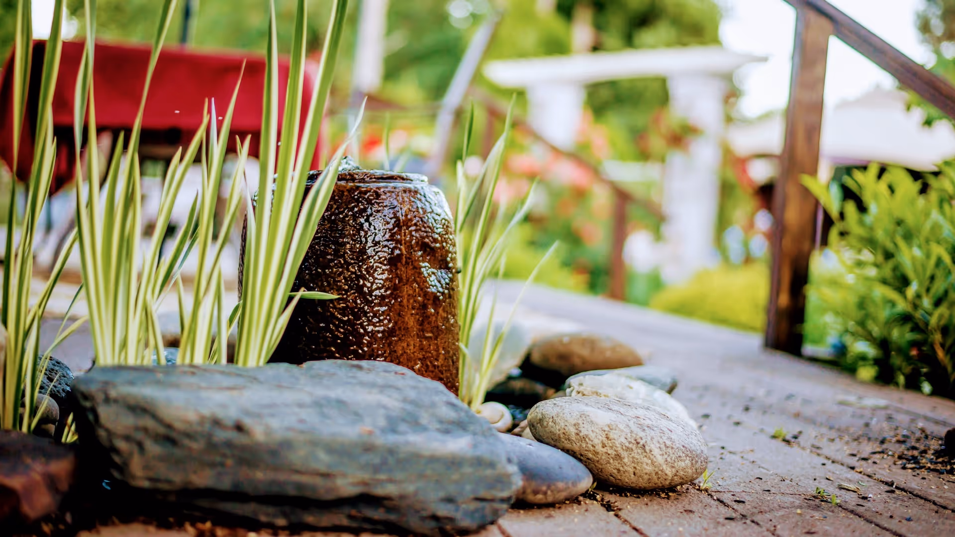 Outdoor garden pathway with rocks, plants, and a wooden railing.