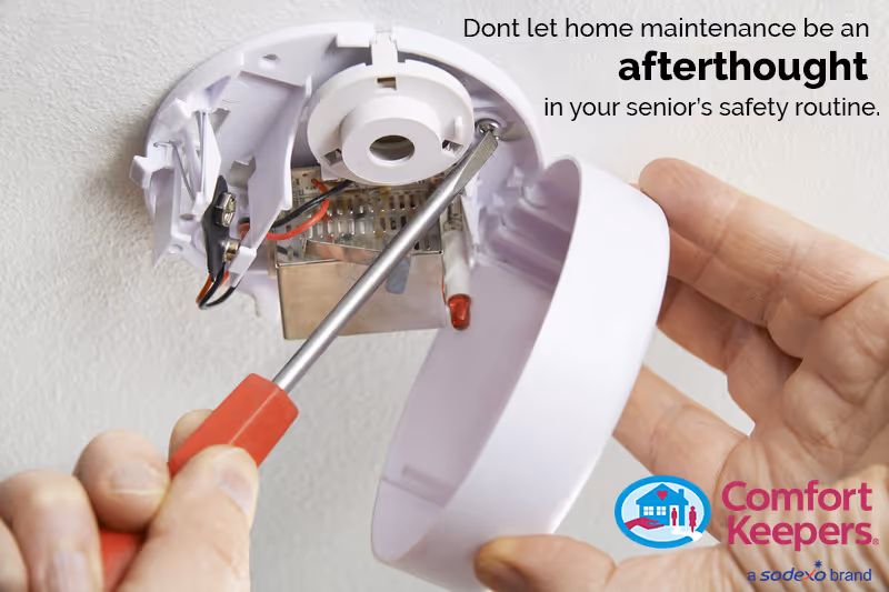 Close-up of hands using a screwdriver to service a wall-mounted smoke detector.