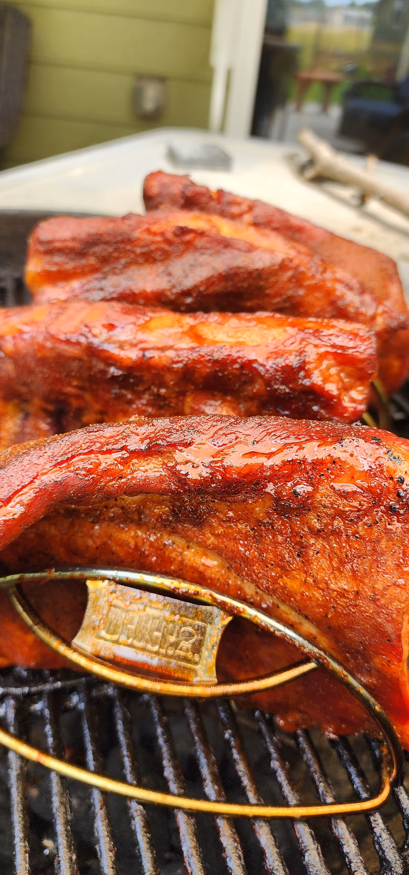 Close-up of glazed barbecue ribs cooking on a grill outdoors.