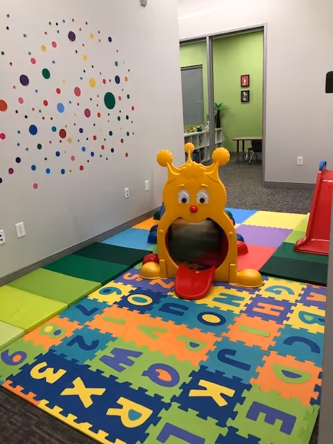 Bright children's play area with a yellow giraffe-shaped play structure and colorful mats.
