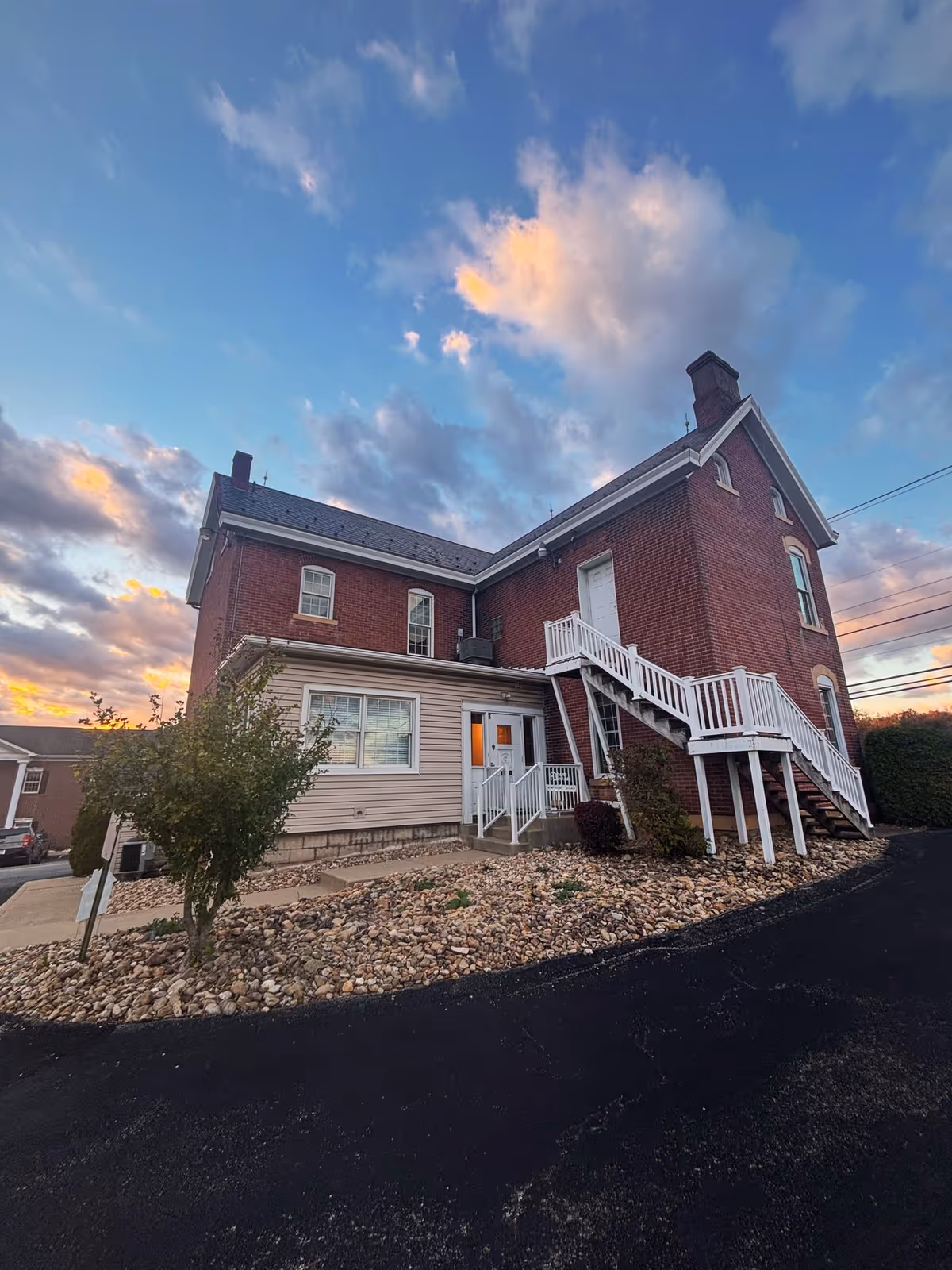 Two-story brick senior living building with white staircases and rocky landscaping at sunset.