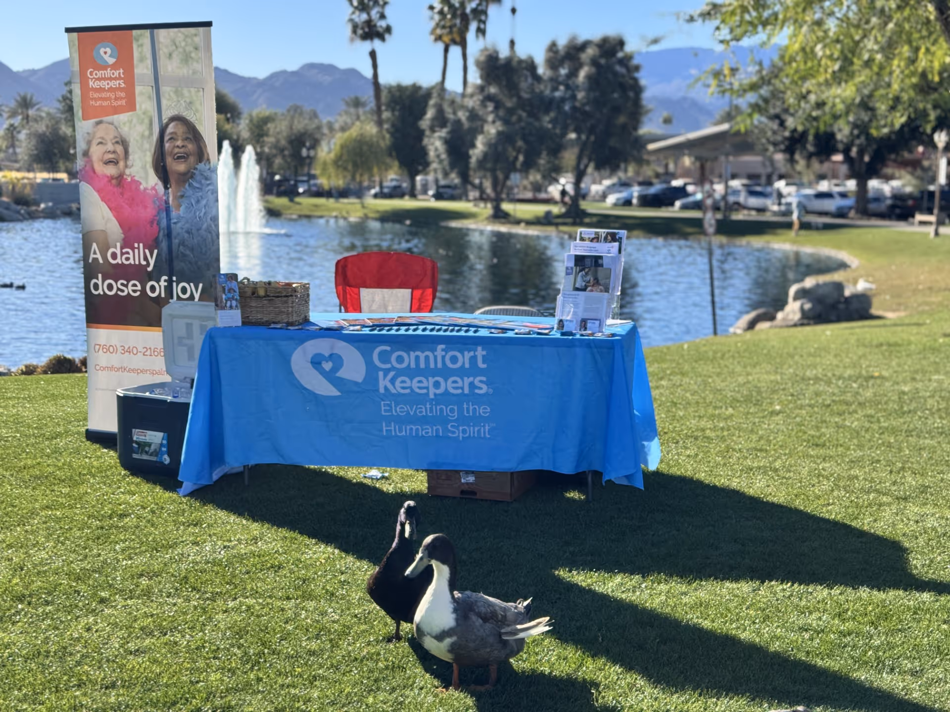 Outdoor promotional table for Comfort Keepers in a park by a pond