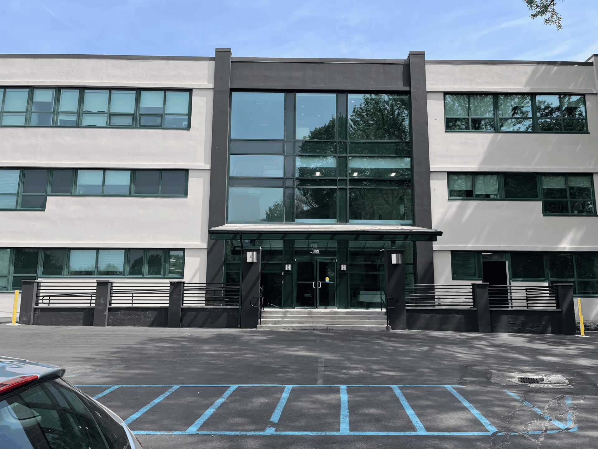 Modern glass-fronted building entrance with a parking lot in front.