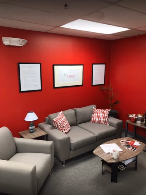 Red-walled lounge area with gray couches, framed certificates, and a coffee table.