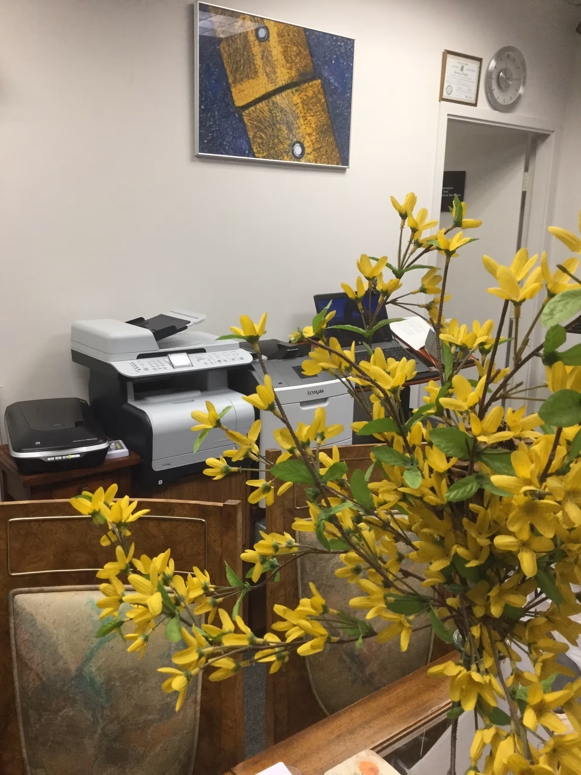 Office area in a senior living facility with a printer and yellow flowers.