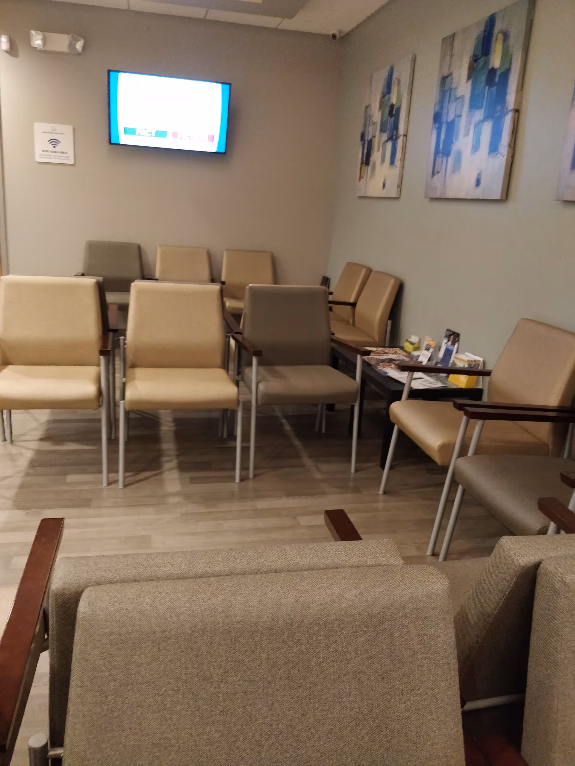 A waiting area with beige chairs, wall art, and a mounted screen.
