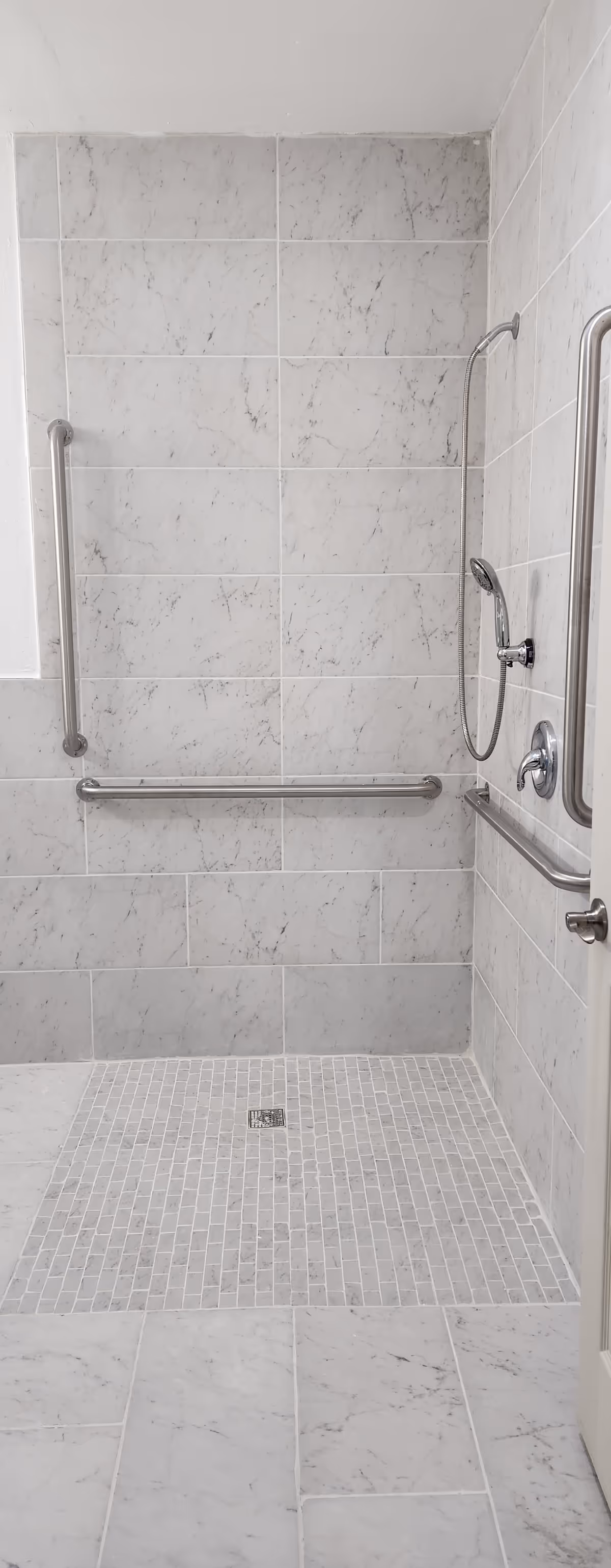 Accessible tiled bathroom shower with multiple grab bars and handheld shower.