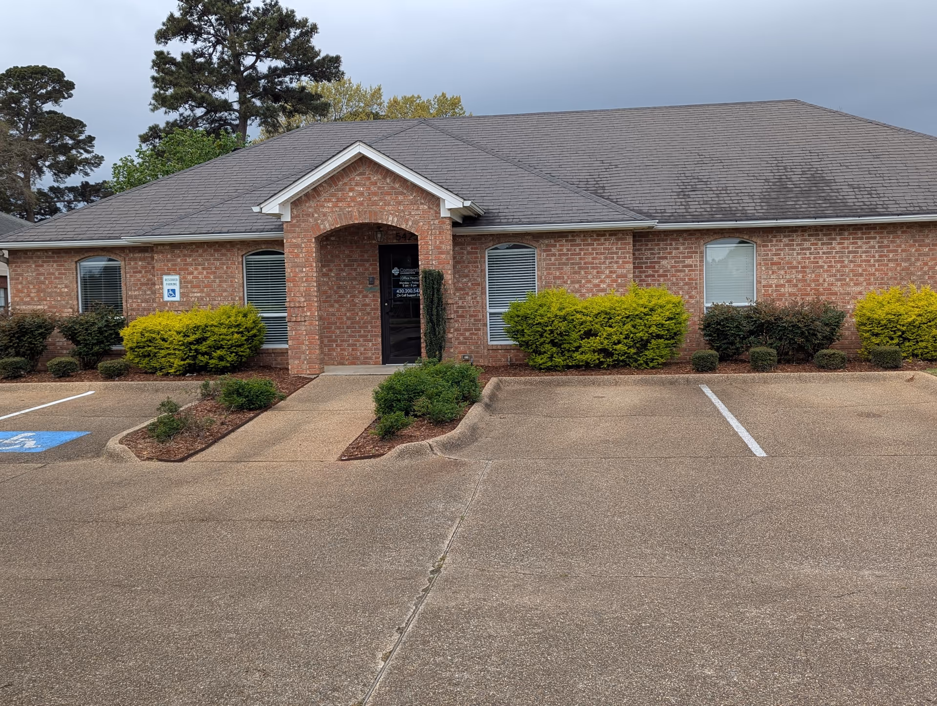 Brick senior living facility exterior with a covered entrance, parking, and shrubs.
