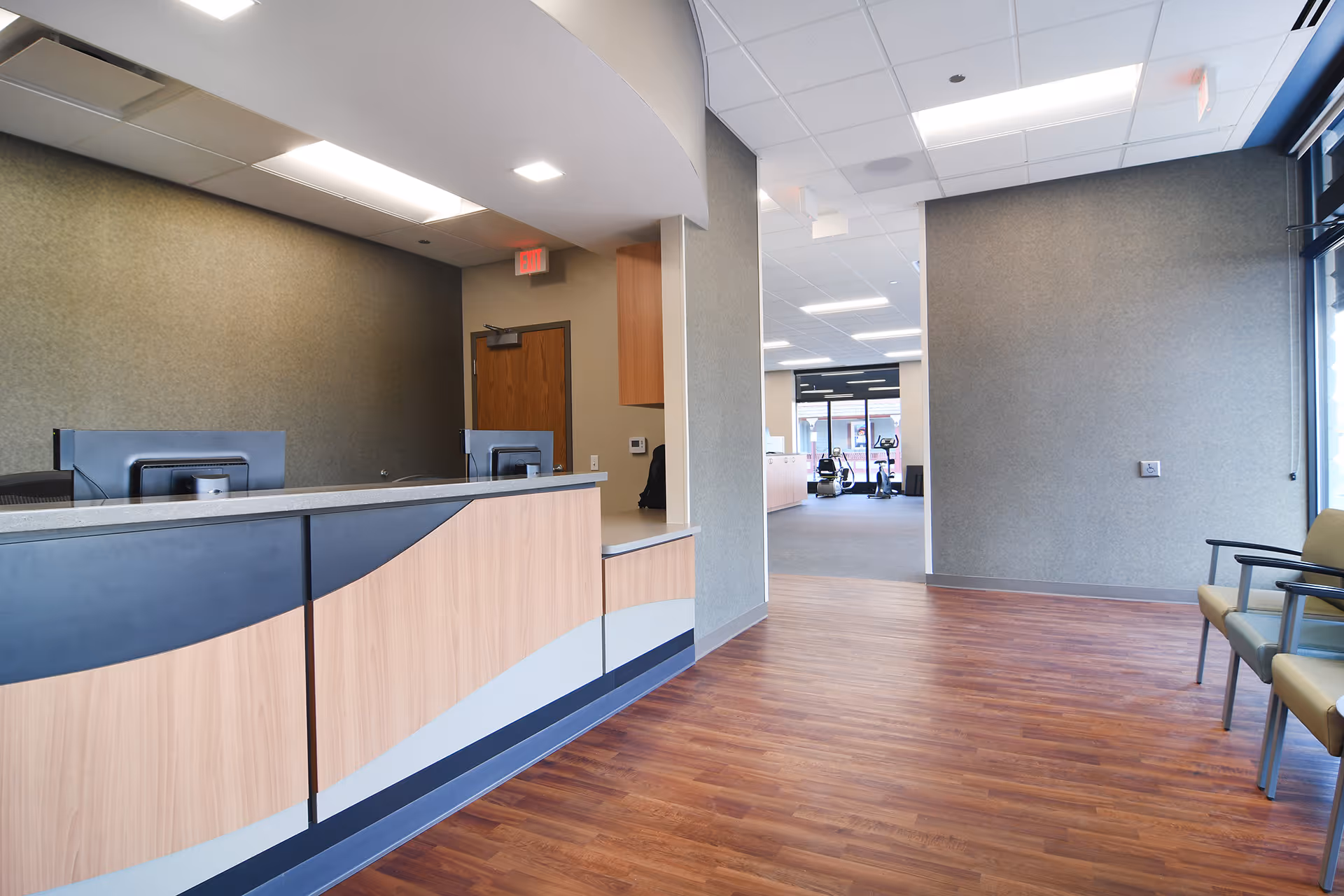 Curved reception desk in a spacious lobby with wood flooring and seating along the wall.