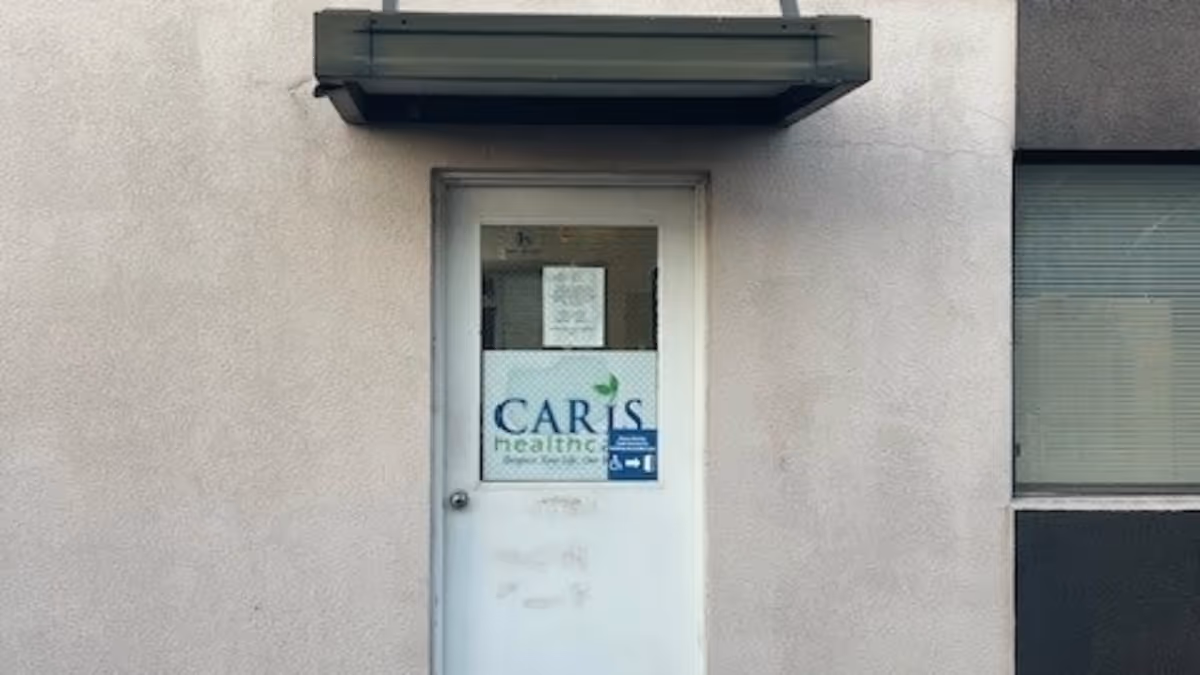 White door with CARIS Healthcare sign set in a gray exterior wall.